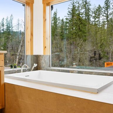 Primary bathroom soaking tub in corner of room with clear windows overlooking river