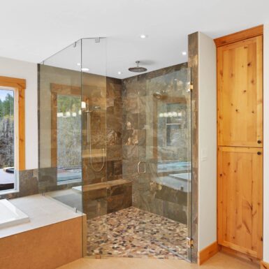 Primary bathroom walk in shower with beautiful floor and wall tile and stone mason work with clear stain wood trim